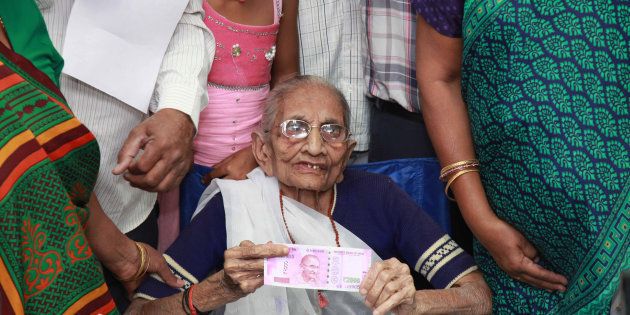 Indian Prime Minister Narendra Modi's mother (C) holds up a 2,000 rupee note after exchanging money at a bank in Rysan village, near Gandhinagar, some 30 kms from Ahmedabad on November 15, 2016.