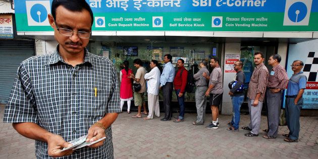 A man counts his money after withdrawing from an ATM even as people are seen waiting in long queues for their money.