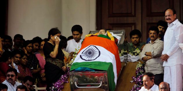Sasikala Natarajan, left standing, a close friend of India's Tamil Nadu state former Chief Minister Jayaram Jayalalithaa, wipes her tears next to Jayalalithaa's body wrapped in the national flag and kept for public viewing outside an auditorium in Chennai.