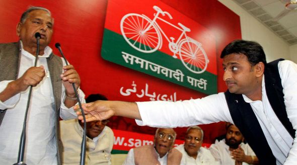 Akhilesh Yadav adjusts microphone for his father, the Samajwadi Party President Mulayam Singh Yadav, during a meeting with the newly elected legislators at party headquarters.