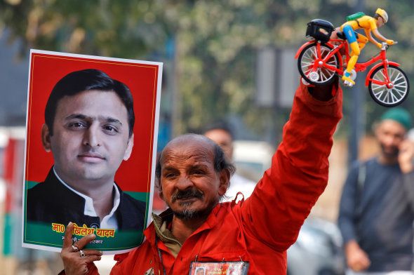 A Samajwadi (SP) party worker holds a toy bicycle representing the party's symbol and a poster of chief minister of Uttar Pradesh Akhilesh Yadav.