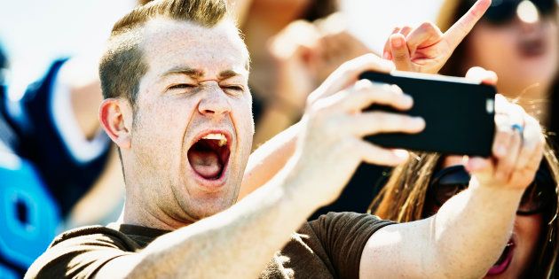 Man celebrating in stadium at football game taking selfie with smartphone