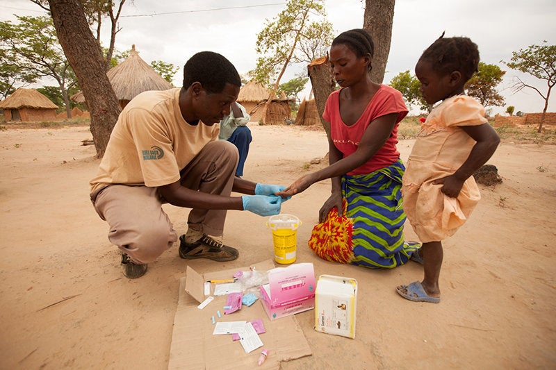 A community health worker administers a rapid diagnostic test on a mother and child for malaria.