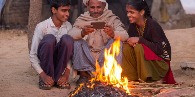 India, Uttar Pradesh, Agra, village man and his two children looking at photos on a smartphone by open fire.