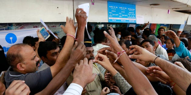 Indians stretch out their hands to collect withdrawal slips from a police officer to deposit and exchange discontinued currency notes