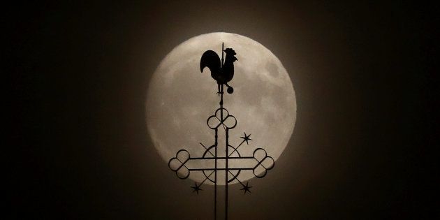 The weathercock of the church of St.Peter and Paul is seen in front of a moon on the eve of the
