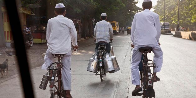 India, Mumbai, two delivery service men (dabbawallahs), and a milkman, riding on bicycles, rear view