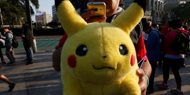 A man carries stuffed toy of a character from Pokemon, Pikachu, as he plays Pokemon Go during a gathering to celebrate
