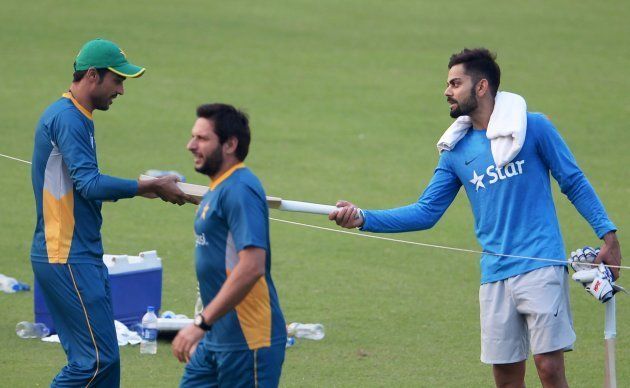 India's Virat Kohli (R) presents a cricket bat to Pakistan's Mohammad Amir (L) as Pakistan's captain Shahid Afridi (C) walks past during a training session at The Eden Gardens Cricket Stadium in Kolkata on March 18, 2016.