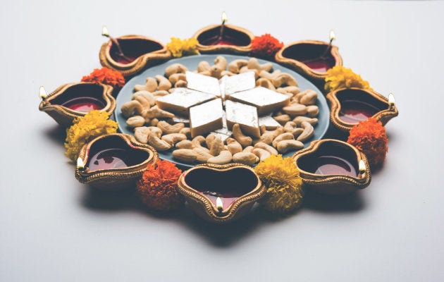 Diwali food Rangoli using Kaju Katli sweet along with Clay diya/lamp and marigold flowers arranged in circular pattern, selective focus