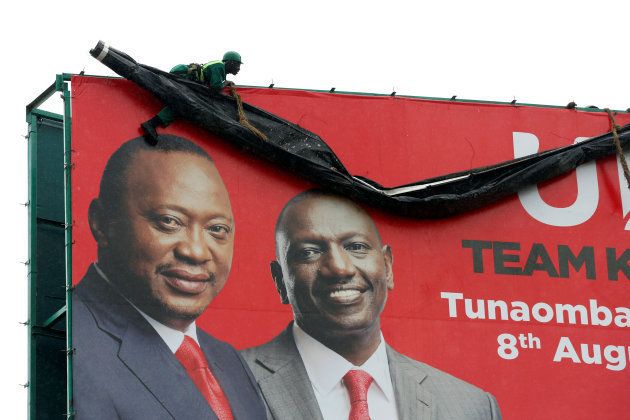 A worker hangs ontop of an election campaign billboard displaying Kenya's President Uhuru Kenyatta (L) and Deputy President William Ruto from the Jubilee Party in the town of Mai Mahiu, Kenya, August 2, 2017.