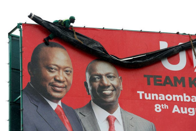 A worker hangs ontop of an election campaign billboard displaying Kenya's President Uhuru Kenyatta (L) and Deputy President William Ruto from the Jubilee Party in the town of Mai Mahiu, Kenya, August 2, 2017.