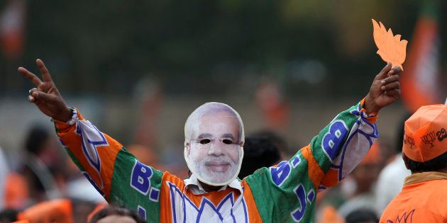 A supporter of Bharatiya Janata Party (BJP) wearing a face mask of Indian Prime Minister Narendra Modi flashes victory sign during an election campaign rally in Bangalore, India, Tuesday, May 8, 2018.