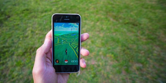Buenos Aires, Argentina - November 11, 2016: Apple iPhone 5c held in one hand showing its screen with Pokemon Go application. Grass on the background.