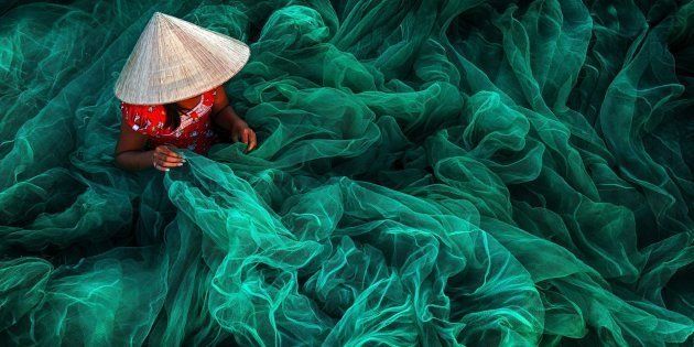 In a small village in southern Vietnam near Phan Rang a woman wearing a typical cone hat is creating a fishing net in their traditional manner The manufacturing of handmade nets is still a typical Vietnamese activity for women which they carry on while their husbands are out fishing