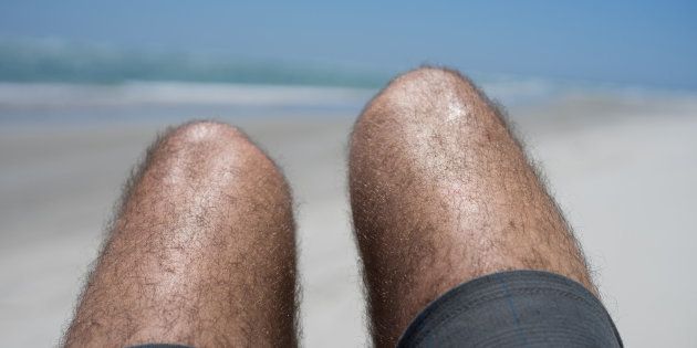 A man with hairy legs and wearing shorts sunbathing with his knees up.