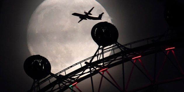 An aeroplane flies past the London Eye wheel, and moon, a day before the
