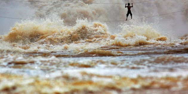 During the rainy season, huge waves dwarf Laotian fisherman Samnieng as he uses a homemade high-wire bridge to cross over the dangerous waters of the turbulent Mekong River in Champasak province, Laos.