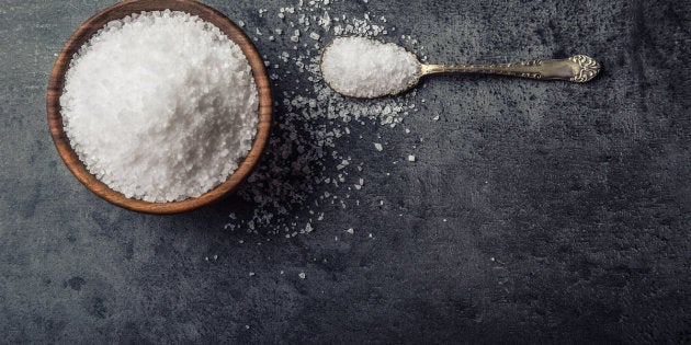 Salt. Coarse grained sea salt on granite - concrete stone background with vintage spoon and wooden bowl.