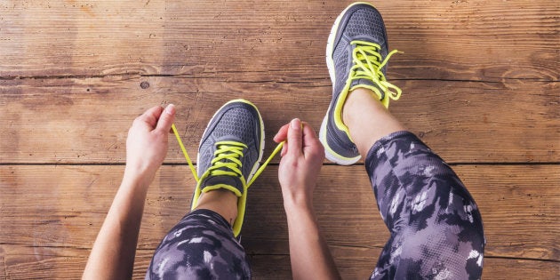 Unrecognizable young runner tying her shoelaces. Studio shot on wooden floor background.