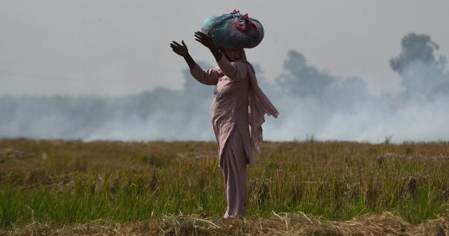 A woman looks on near burning straw stubble at a field in Barana village.