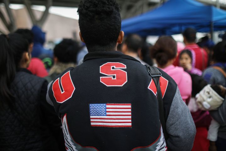 A man in a "USA" jacket waits with migrants at the El Chaparral border crossing to hear names called out on Nov. 28.