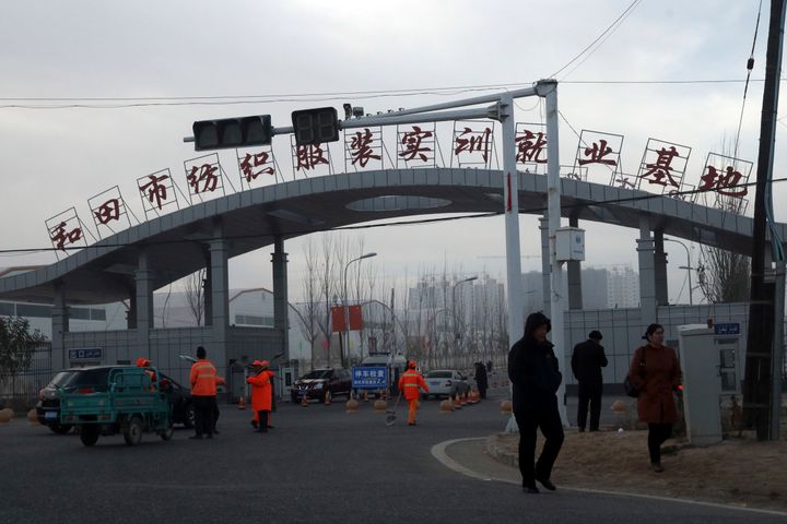 In this Wednesday, Dec. 5, 2018, photo, residents pass by the entrance to the "Hotan City apparel employment training base" where Hetian Taida has a factory in Hotan in western China's Xinjiang region. 
