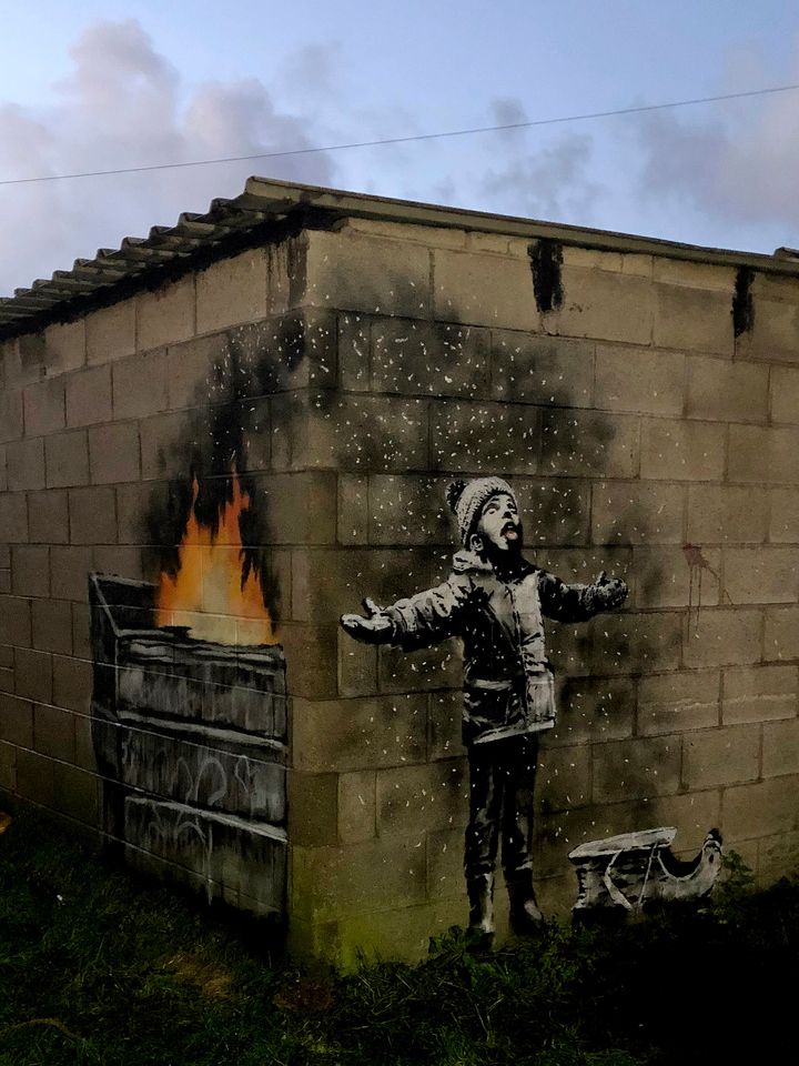 The full mural by Banksy reveals that the child is standing in ash from a dumpster fire.