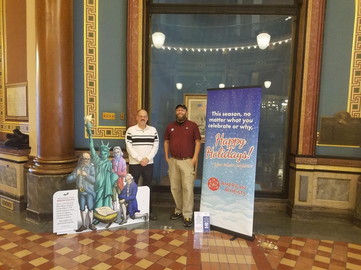 A holiday banner from the American Atheists (right) stands next to an alternative nativity display from the Freedom From Religion Foundation at the Iowa State Capitol building.