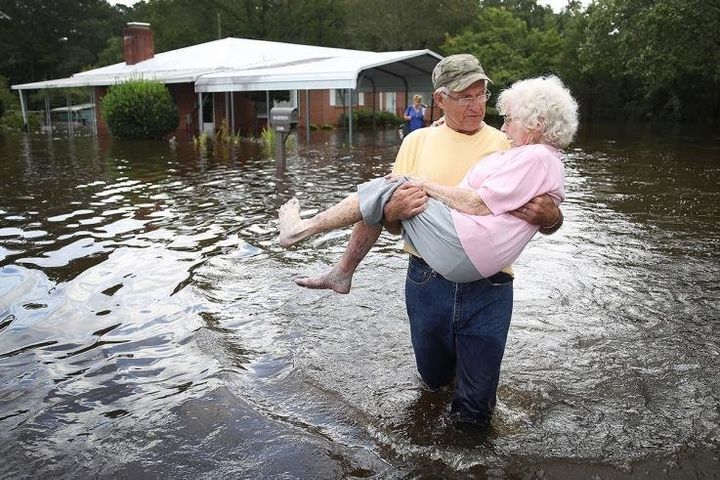 Ένας άνδρας μεταφέρει στα χέρια του τη συζυγό του, αντιμέτωπος με τα νερά της καταστροφής