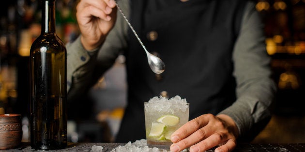 Barman stirring cachaca with lime and ice in the glass making Caipirinha cocktail on the bar counter