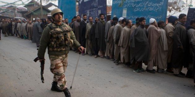 An Indian paramilitary soldiers walks past Kashmiri voters standing in queue outside a polling station during the first phase of voting to the Jammu and Kashmir state assembly elections in Lar, some 30 kilometers (19 miles) north of Srinagar, Indian controlled Kashmir, Tuesday, Nov. 25, 2014. The five phased voting is scheduled to be held till December 20 with the results expected on December 23. (AP Photo/ Dar Yasin)