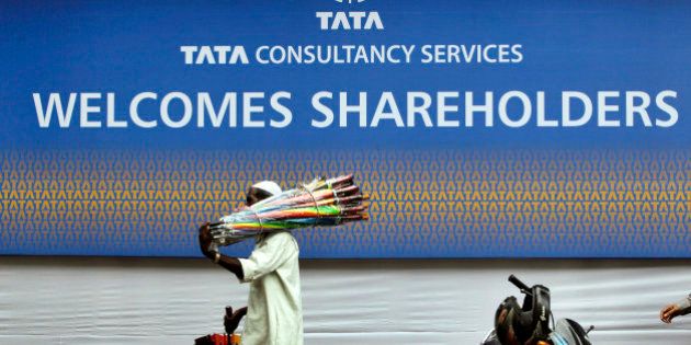 An umbrella seller walks in front of Tata Consultancy Services signboard on the day of its annual general meeting in Mumbai, India, Friday, June 29, 2012. (AP Photo/Rajanish Kakade)