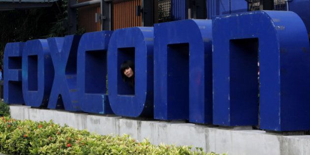A worker looks out through the logo at the entrance of the Foxconn complex in the southern Chinese city of Shenzhen Thursday, May 27, 2010. A young man became the 10th worker to jump to his death at a Foxconn Technology Group factory in the city, just hours after the company's chairman toured the plant that makes iPods and other top-selling gadgets, state-run media said. (AP Photo/Kin Cheung)