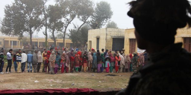 Indian paramilitary soldiers stand guard, as people stand in queues to cast their votes outside a polling station during the fifth phase of voting, at Satrayan village near the India-Pakistan international border, about 32 kilometers from Jammu, India, Saturday, Dec. 20, 2014. The fifth and last stage of polling is being held in Jammu and Kashmir state and Jharkhand. (AP Photo/Channi Anand)