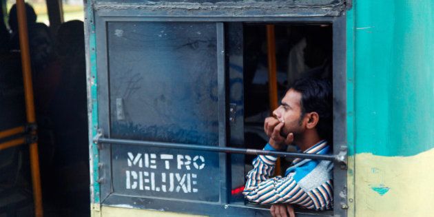[UNVERIFIED CONTENT] Young man traveling in a typical old bus in Hyderabad, Andhra Pradesh, India. He is looking ahead out from the window. Thoughtful, dreamy look. 'Metro deluxe' sign on the bus.