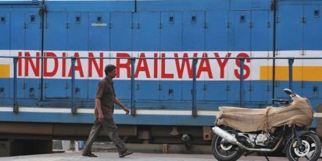 An Indian man walks in front of a train as a motorcycle being transported is kept on a platform at the Secunderabad railway station in Hyderabad, India, Monday, July 7, 2014. India on Tuesday is expected to announce the budget for the national railways system, which is one of the world's largest and serves 23 million passengers a day. (AP Photo/Mahesh Kumar A.)