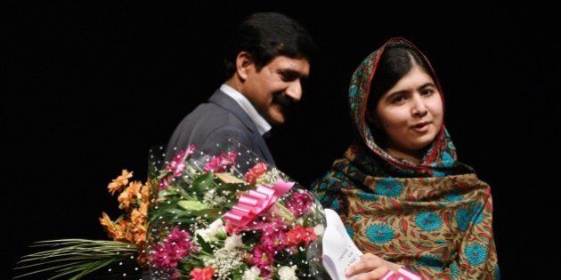 Pakistani rights activist Malala Yousafzai, stands with her father Ziauddin Yousafzai as she holds bouquets of flowers after addressing the media in Birmingham, central England on October 10, 2014. The Nobel Peace Prize went Friday to 17-year-old Pakistani Malala Yousafzai and India's Kailash Satyarthi for their work promoting children's rights. Seventeen-year-old Nobel Peace Prize winner Malala Yousafzai said she was 'honoured' to be the first Pakistani and the youngest person to be given the award and dedicated the award to the 'voiceless'. 'This award is for all those children who are voiceless, whose voices need to be heard,' she said. AFP PHOTO / OLI SCARFF (Photo credit should read OLI SCARFF/AFP/Getty Images)