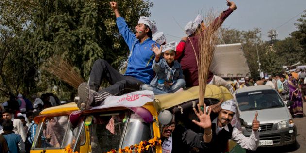 Supporters of the Aam Aadmi Party, or Common Manâs Party, shout slogans as they sit on an autorickshaw decorated with brooms, the party symbol, outside the venue where party leader Arvind Kejriwal is being sworn-in as the new chief minister of Delhi, in New Delhi, India, Saturday, Feb. 14, 2015. Kejriwal and the party he created routed the country's best-funded and best-organized political machine and dealt an embarrassing blow to Prime Minister Narendra Modi. (AP Photo/Bernat Armangue)