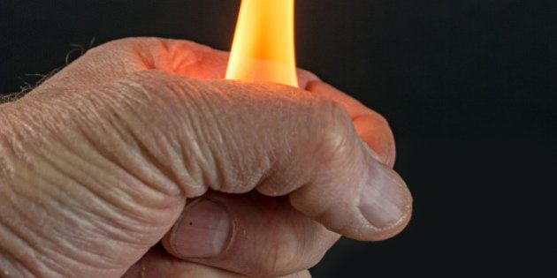A man's hand holding a large yellow flame with a black background.