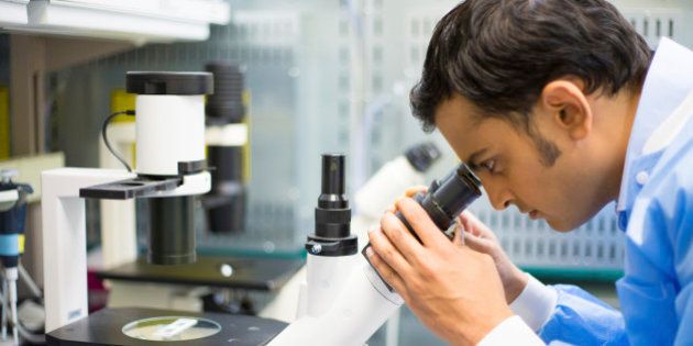 Closeup portrait, young scientist in blue gown looking into microscope. Isolated lab background. Research and development.