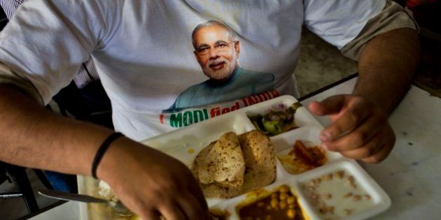 A supporter wears a t-shirt with a portrait of Bharatiya Janata Party (BJP) leader and Indiaâs next prime minister Narendra Modi and eats a meal at the canteen of the BJP party office in New Delhi, Friday, May 16, 2014. Modi and his party won national elections in a landslide Friday, preliminary results showed, driving the long-dominant Congress party out of power in the most commanding victory India has seen in more than a quarter century. Writing on banner reads