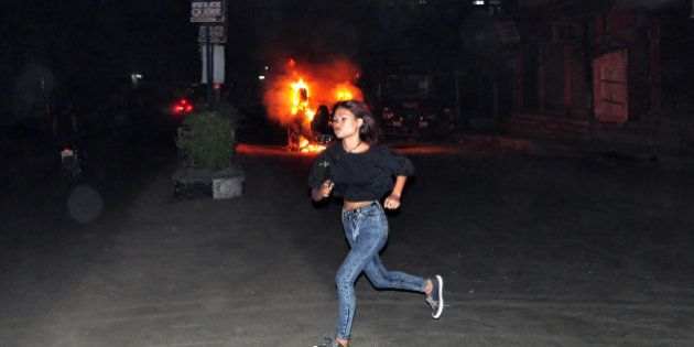 In this Thursday, March 5, 2015 photo, an unidentified girl runs in front of a car set on fire by a mob, during clashes with police following the lynching of a man accused of rape in Dimapur, India, in the northeastern Indian state of Nagaland. Several thousand people overpowered security at Dimapur Central Prison in Nagaland on Thursday, where they dragged away a man accused of rape and then lynched him, police said Friday. (AP Photo/Imojen I Jamir)