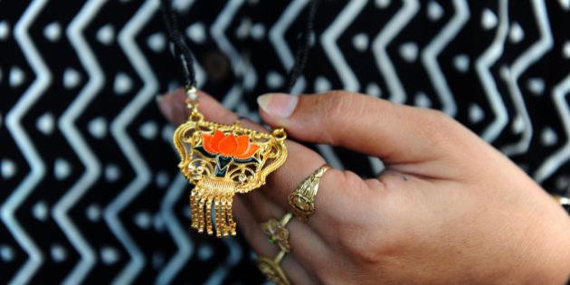 An unidentified Indian married woman admires a mangalsutra made of brass and featuring the symbol of the Bharatiya Janta Party (BJP) for sale on the stall of electoral publicity dealer Prakashbhai Naik in Ahmedabad on April 15, 2009. Naik sells Mangalsutra at Indian Rupees 25 (US 50 cents) each. A mangalsutra is an Indian symbol of Hindu marriage, consisting of a gold ornament strung from a yellow thread, a string of black beads or a gold chain. It is comparable to a Western wedding ring, and is worn by a married woman until her husband's death. As many as 5,000 mangalsutras, made of brass, will be distributed in each of the 26 electoral constituencies in the westenr Indian state of Gujarat. India will hold its fifteenth parliamentary general elections in five phases on April 16, April 23, April 30, May 7,and May 13 and the new parliament will be constituted before June 2. AFP PHOTO/ Sam PANTHAKY (Photo credit should read SAM PANTHAKY/AFP/Getty Images)