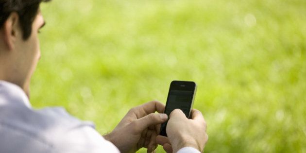 A businessman sitting on the grass, using his mobile phone