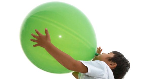 boy blowing up a big green balloon