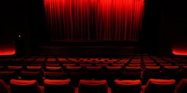 Darkened, empty cinema auditorium with red curtain covering screen, and red chairs.