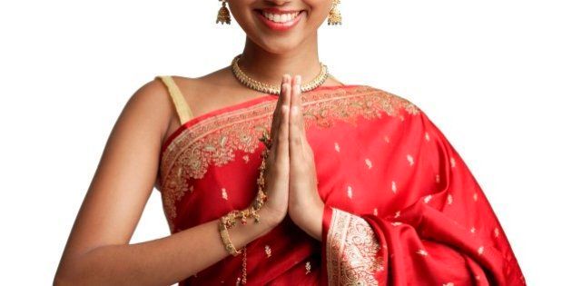 Woman in traditional Indian costume, standing with hands together, smiling at camera
