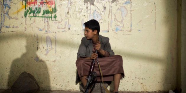 A boy holds his weapon, as he sits on guard near the site of a protest against Saudi-led airstrikes in Sanaa, Yemen, Friday, April 10, 2015. Pakistani lawmakers on Friday unanimously voted to stay out of the Saudi-led air coalition targeting Shiite rebels in Yemen in a blow to the alliance, while planes loaded with badly needed medical aid landed in Yemen's embattled capital, Sanaa, in the first such deliveries since the airstrikes started more than two weeks ago. (AP Photo/Hani Mohammed)