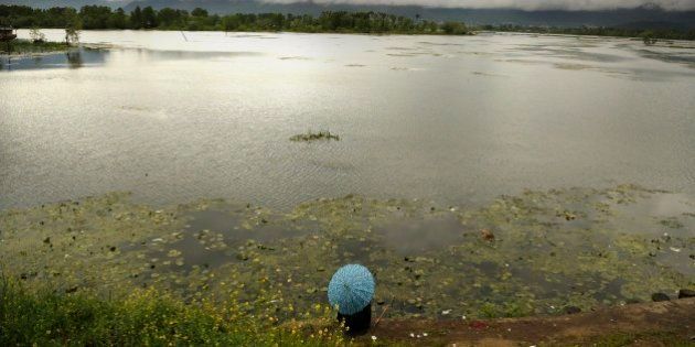 A Kashmiri man holds an umbrella as he fishes sitting on the banks of the Nigeen Lake on a rainy day in Srinagar, Indian controlled Kashmir, Monday, April 27, 2015. (AP Photo/Mukhtar Khan)